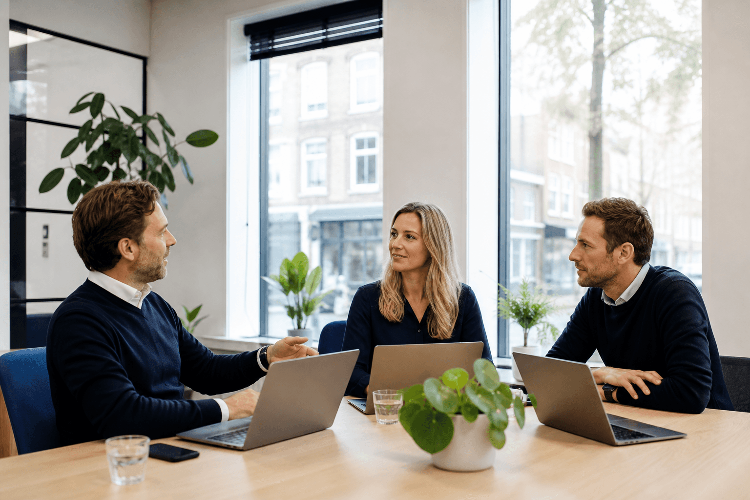 Collega’s in een moderne MKB-werkplek overleggen achter laptops